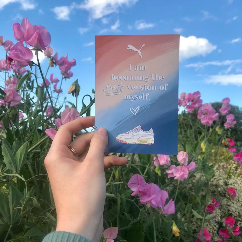 Hand holding a motivational card with a Puma logo against a floral background