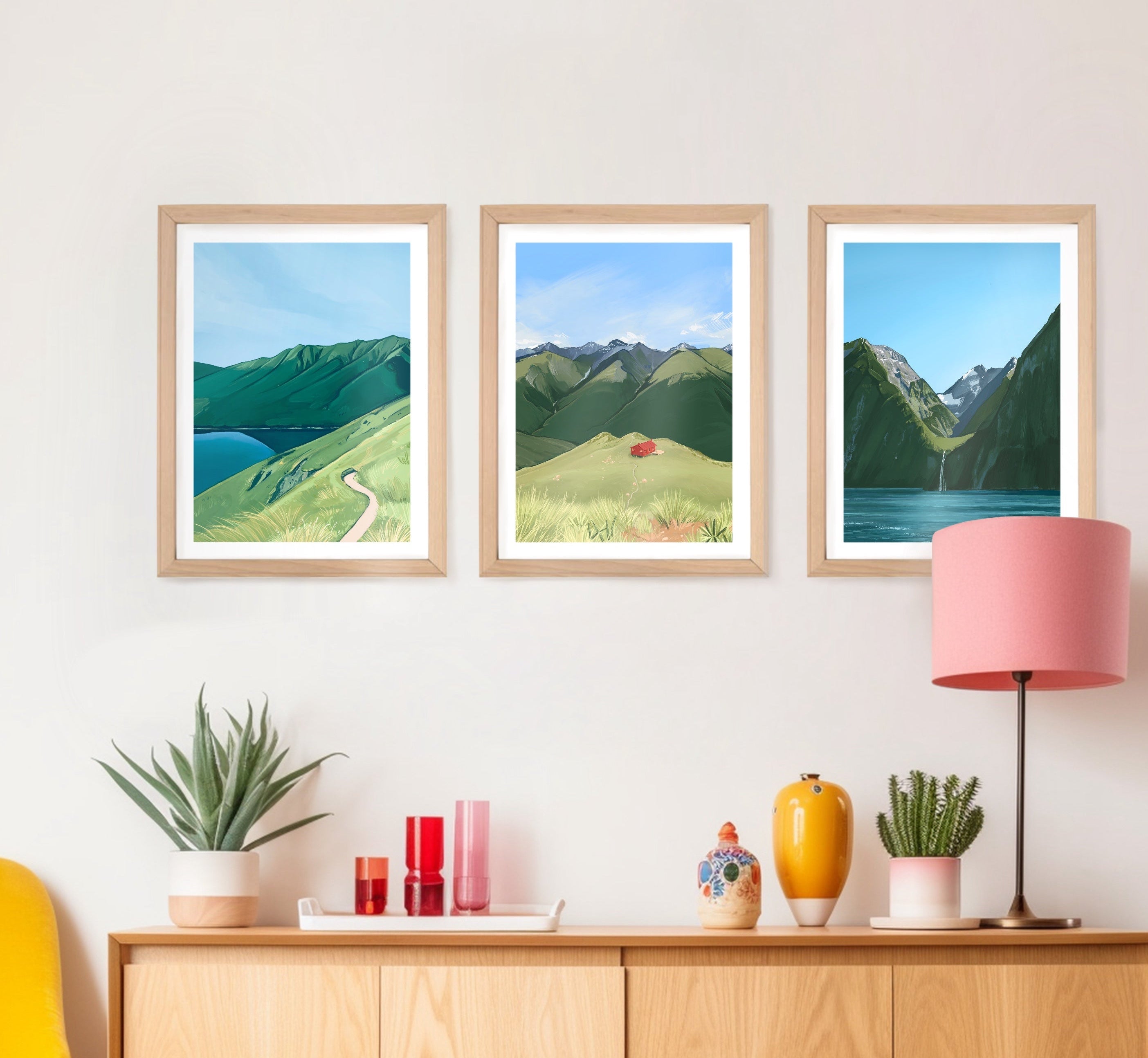 Three framed landscape pictures on a wall above a wooden cabinet with decorative items.